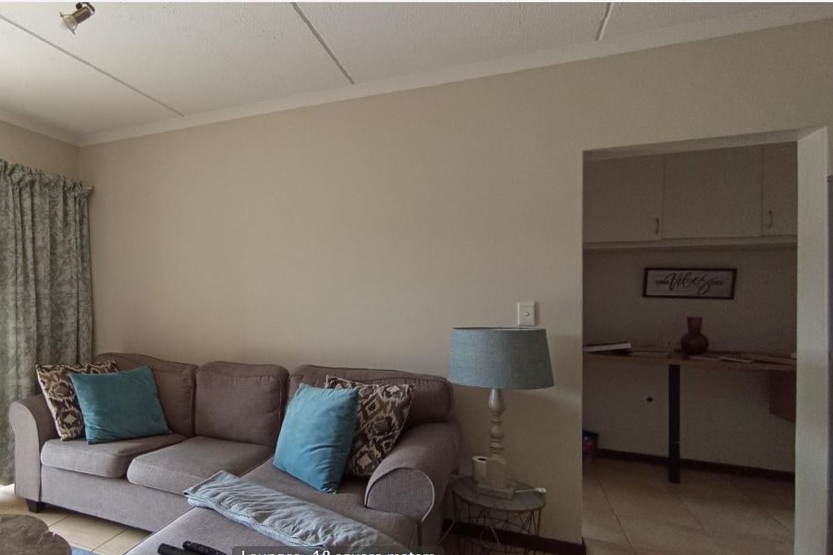 A living room area featuring tiled flooring and a view into an adjacent kitchen or scullery space with built-in cabinetry.