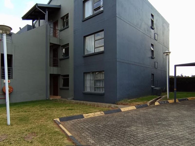 Exterior view of a modern multi-story apartment complex featuring paved parking areas, landscaped grounds, and contemporary dark-toned facade finishes.