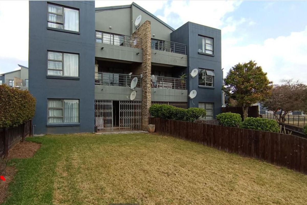 Rear view of a multi-story apartment building featuring private balconies, stone accents, metal security gates, and a private garden area with timber fencing.