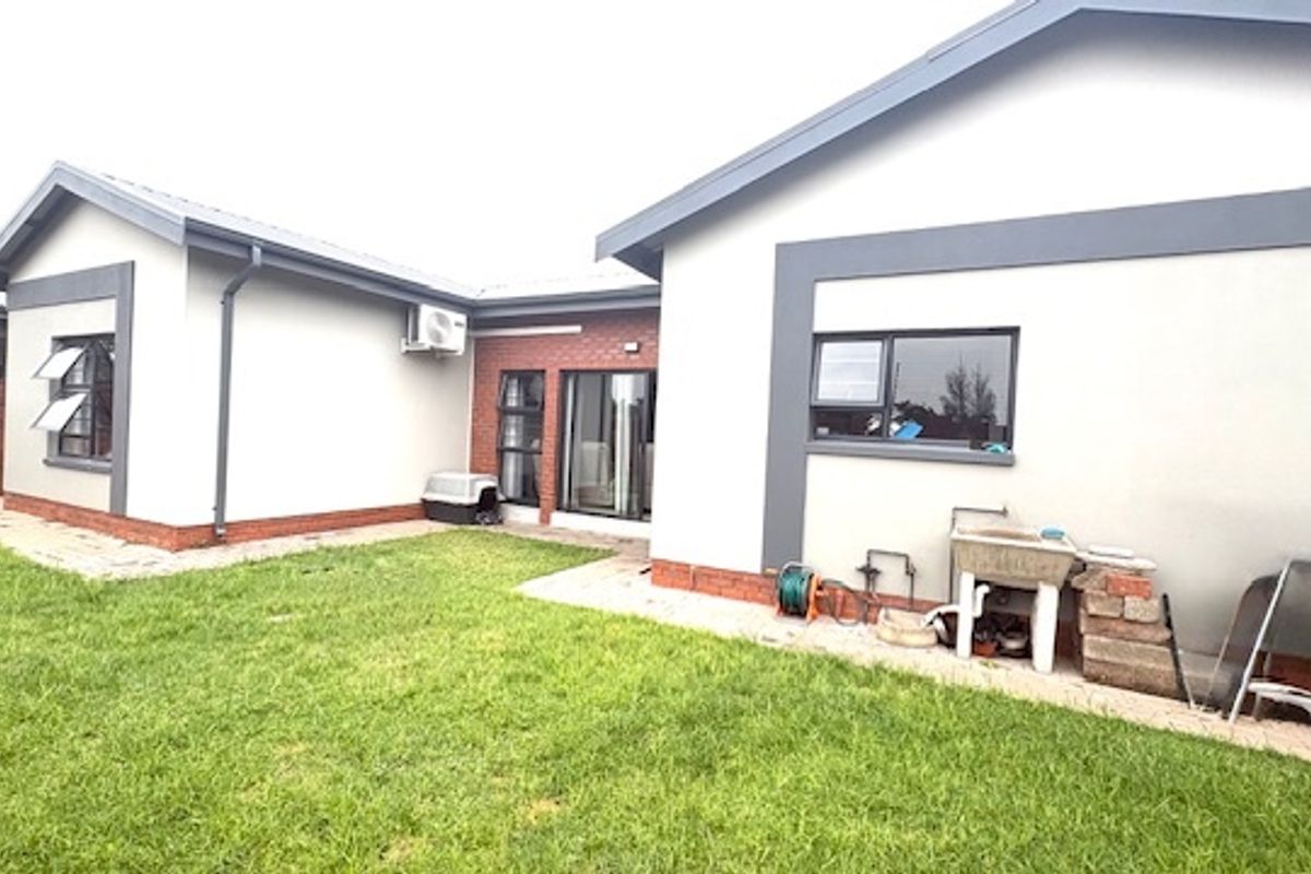 Rear view of the townhouse featuring a private lawn, concrete patio area, and external utility sink with access via sliding glass doors.