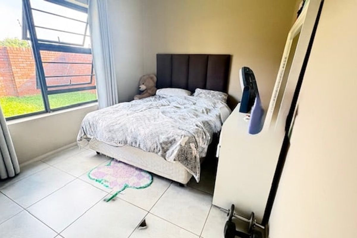 A bedroom featuring tiled flooring and a large top-hung window providing natural light and views of the exterior brick wall.