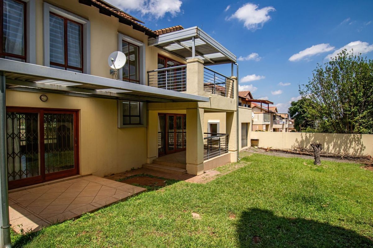 Rear view of the property featuring a tiled patio, an upper-level balcony with metal pergola, and a private garden area.