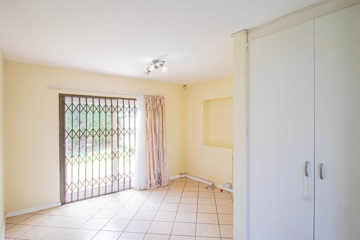 An empty living area featuring tiled flooring, a built-in cupboard, and a sliding door with a security gate leading to the garden.