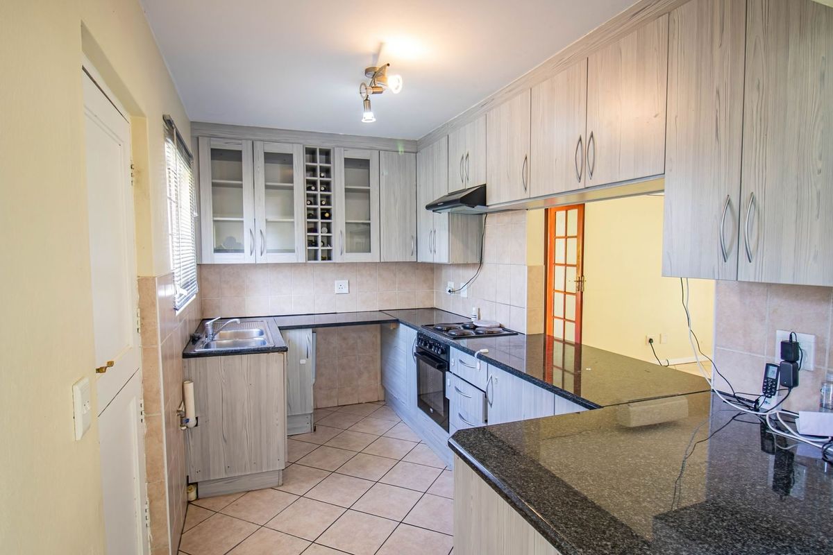 A functional kitchen featuring light wood-grain cabinetry, dark granite countertops, built-in oven and hob, and tiled flooring with a neutral backsplash.