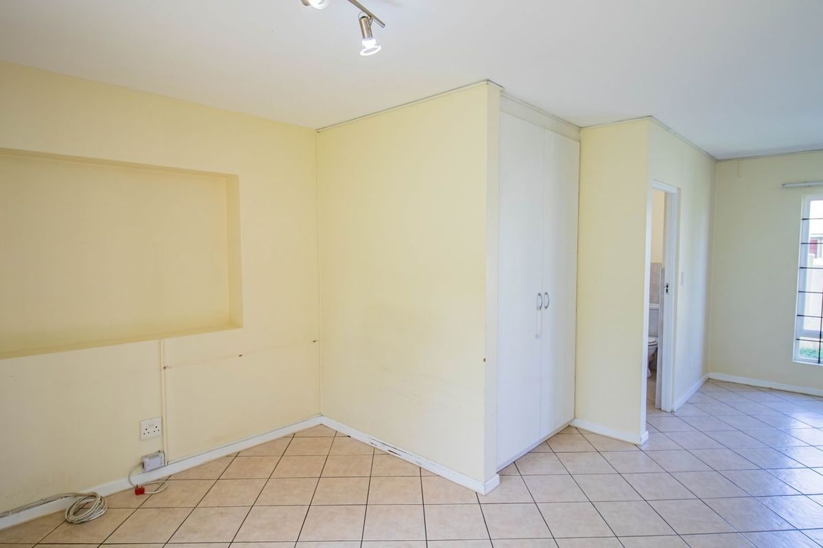 An empty bedroom featuring tiled flooring, a built-in cupboard, and a recessed wall niche, offering a blank canvas for personalization.
