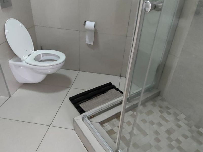 Modern bathroom featuring a wall-mounted toilet and a glass-enclosed shower with tiled flooring and neutral wall finishes.