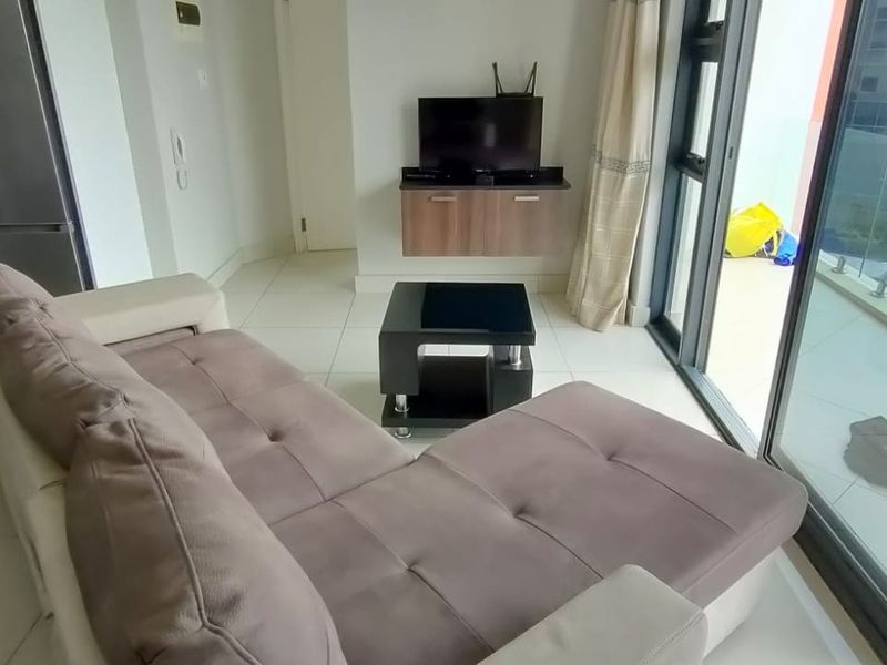 Open plan living area featuring tiled flooring, large sliding glass doors leading to a balcony, and a compact kitchen area with built-in cabinetry.