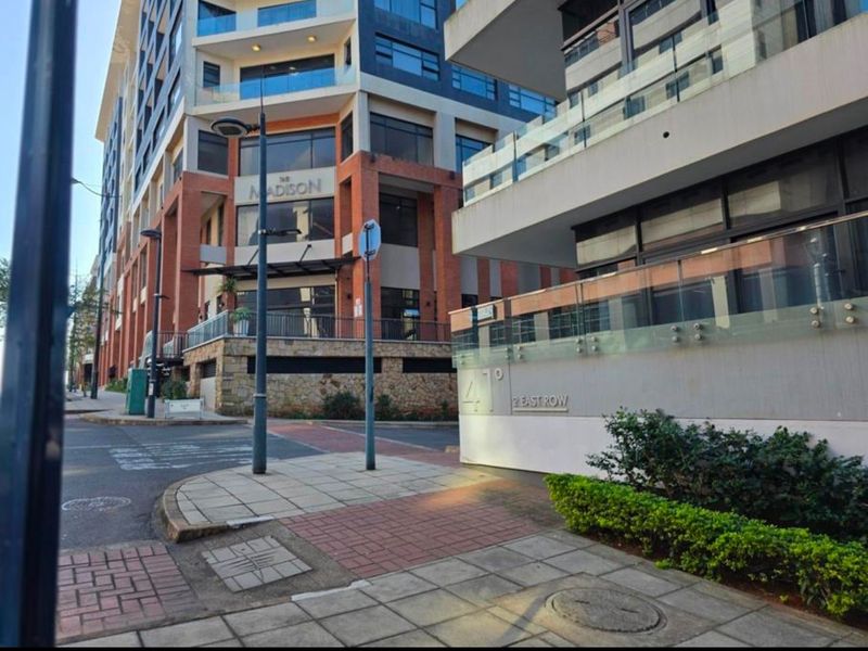 Street-level view of The Madison apartment complex, showcasing modern architectural design, glass balcony railings, and paved pedestrian access.