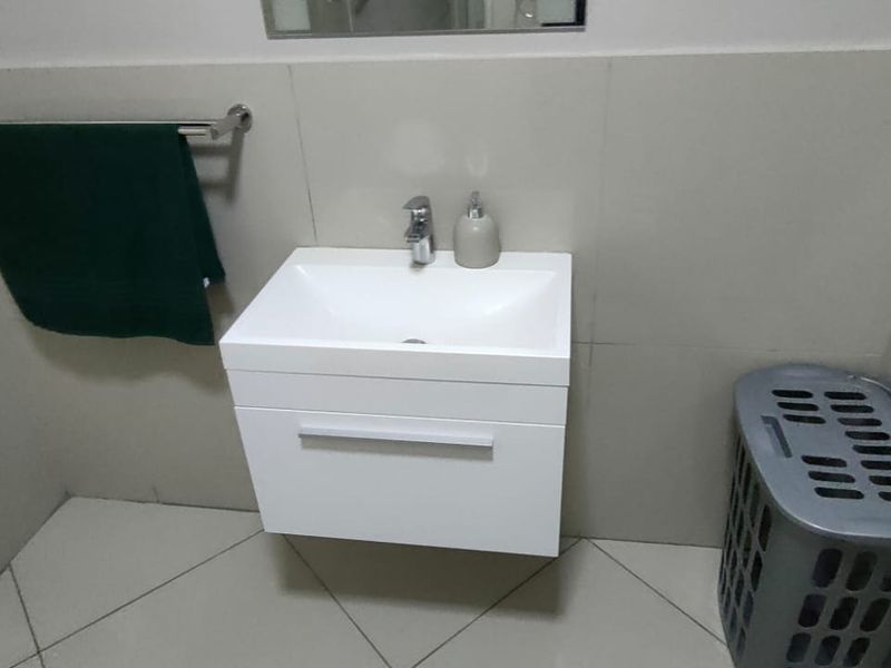 A modern bathroom featuring a wall-mounted vanity with a white basin and chrome faucet, complemented by neutral wall and floor tiling.