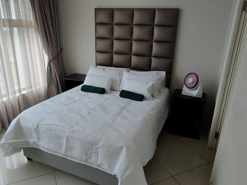 A well-maintained bedroom featuring large windows with floor-to-ceiling curtains and tiled flooring.