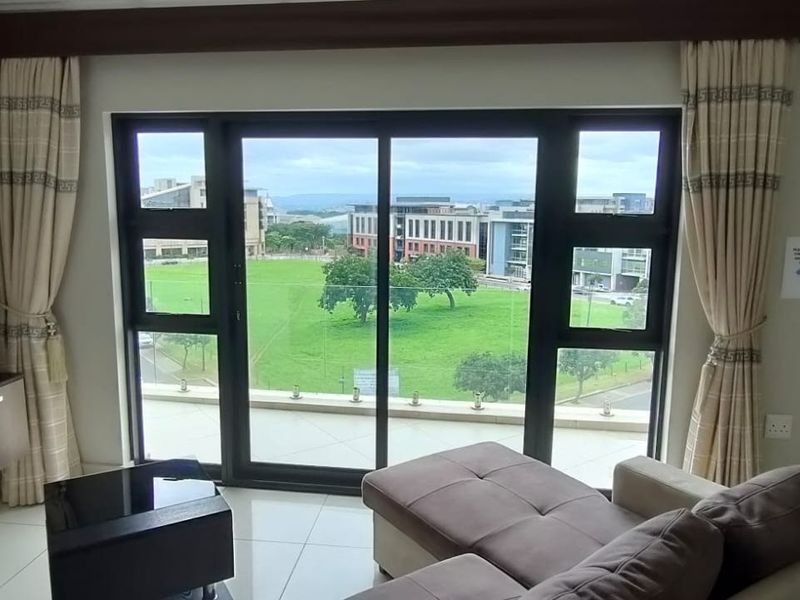 A bright living room featuring large sliding glass doors that open onto a balcony, offering expansive views of the surrounding green landscape.