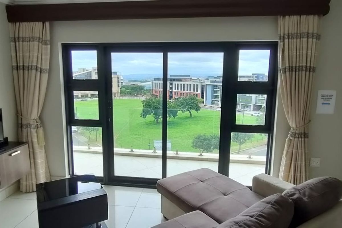A bright living room featuring large sliding glass doors that open onto a balcony, offering expansive views of the surrounding green landscape.