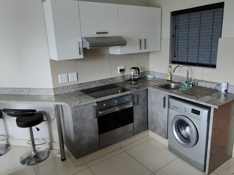 Compact modern kitchen featuring granite countertops, built-in oven, hob, extractor fan, and integrated laundry appliance space.