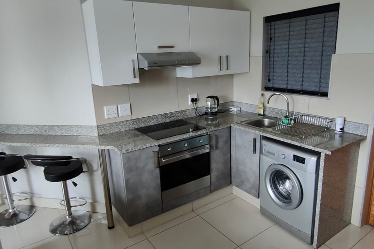 Compact modern kitchen featuring granite countertops, built-in oven, hob, extractor fan, and integrated laundry appliance space.