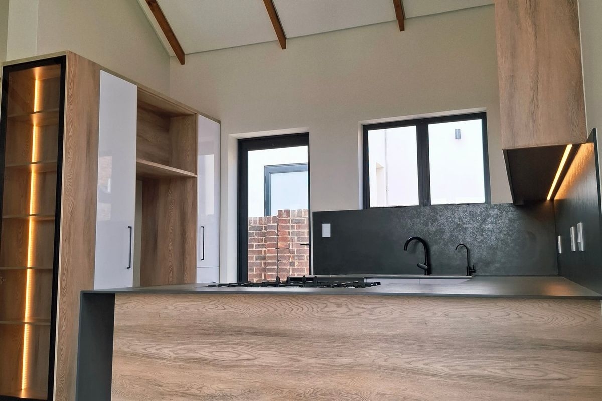 Modern kitchen featuring wood-grain cabinetry, a central island with a gas hob, integrated lighting, and a high vaulted ceiling with exposed timber beams.