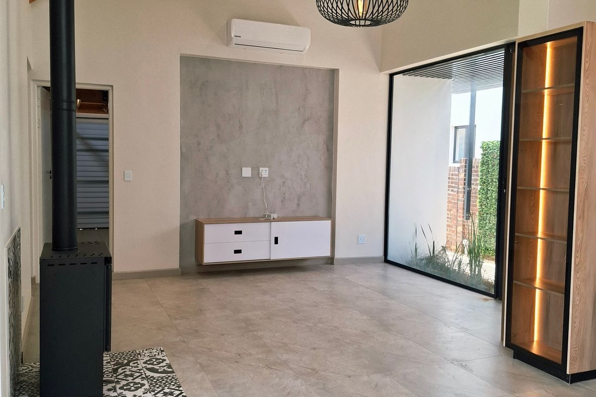 Spacious living area featuring a vaulted ceiling with exposed timber rafters, tiled flooring, a modern freestanding fireplace, and large glass doors leading outdoors.