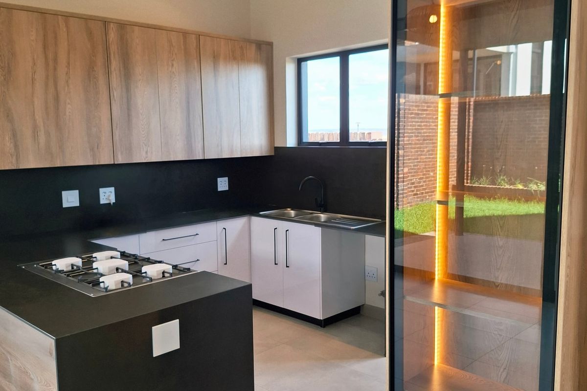 Modern kitchen featuring sleek cabinetry, a gas hob, integrated display shelving, and a vaulted ceiling with exposed timber beams.