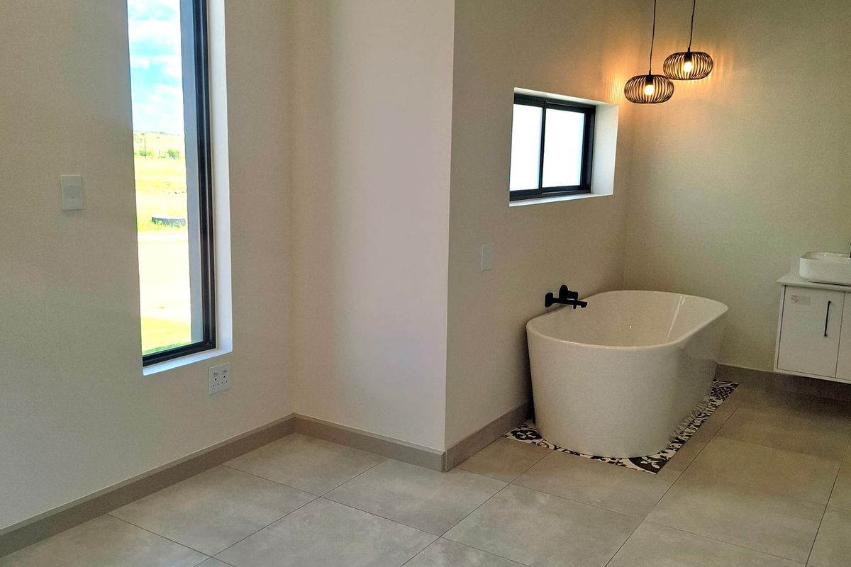Modern bathroom featuring a sleek freestanding bathtub, vanity cabinet with basin, large windows, and contemporary tiled flooring.