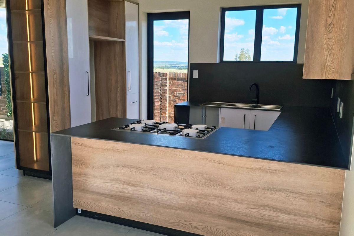 Modern kitchen featuring wood-grain cabinetry, a gas hob, double sink, and vaulted ceilings with exposed timber beams, offering a bright and contemporary aesthetic.