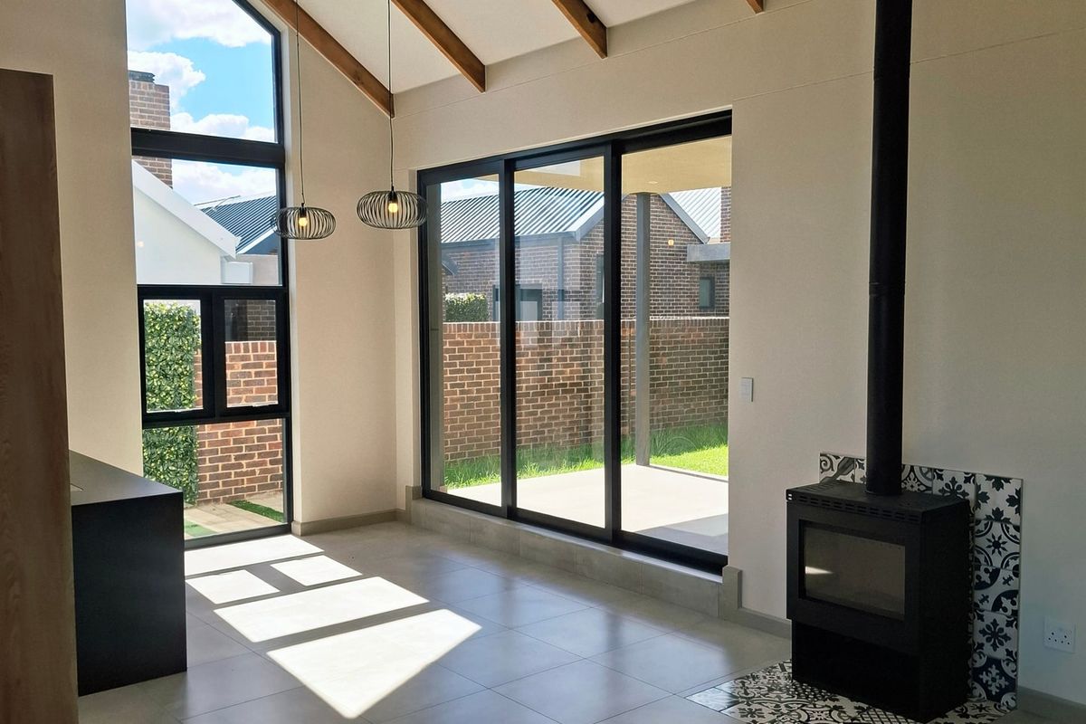 Spacious living area featuring high vaulted ceilings with exposed timber beams, a modern freestanding fireplace, and large glass doors opening to the rear garden.
