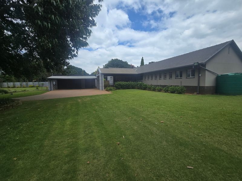 Spacious rear exterior view featuring a large manicured lawn, paved driveway, double garage, and a water tank attached to the main house structure.