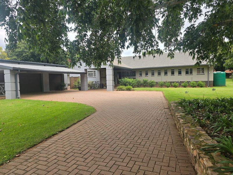 Front view of the property featuring a spacious paved driveway, double garage, well-maintained lawn, and stone retaining wall.
