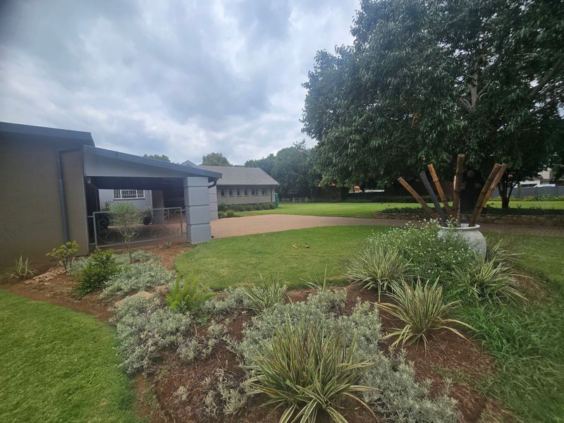 A spacious rear garden featuring a covered patio area, paved driveway, and well-maintained landscaping with mature trees.