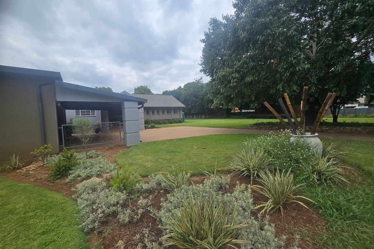 A spacious rear garden featuring a covered patio area, paved driveway, and well-maintained landscaping with mature trees.
