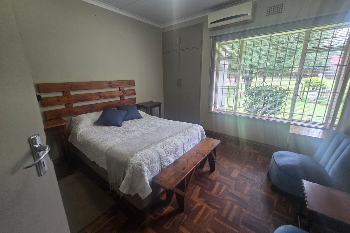 A well-maintained bedroom featuring classic parquet flooring, built-in storage cupboards, and a wall-mounted air conditioning unit for climate control.