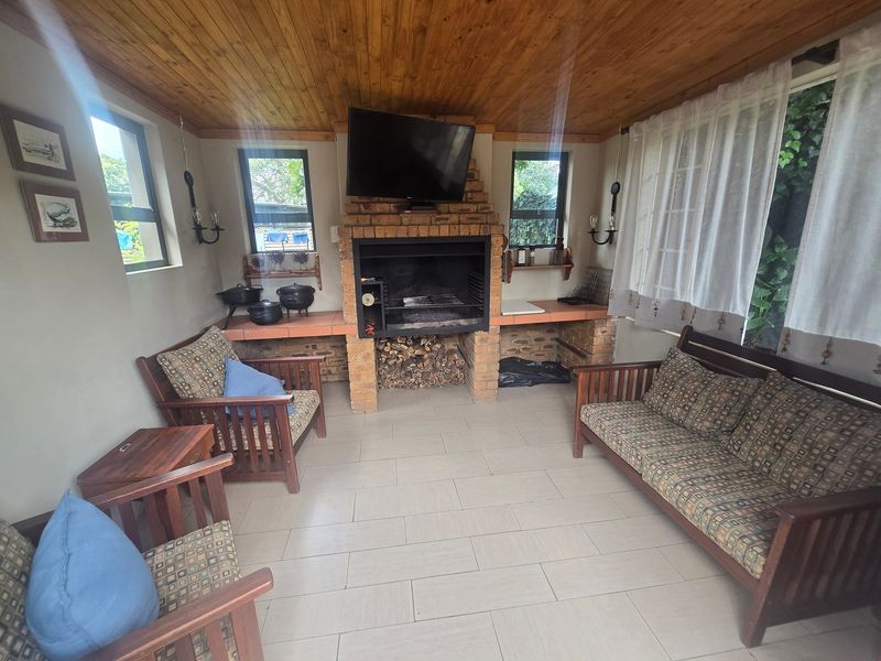 Covered patio area featuring a built-in brick braai, timber ceiling, and tiled flooring, providing a functional space for outdoor entertaining.