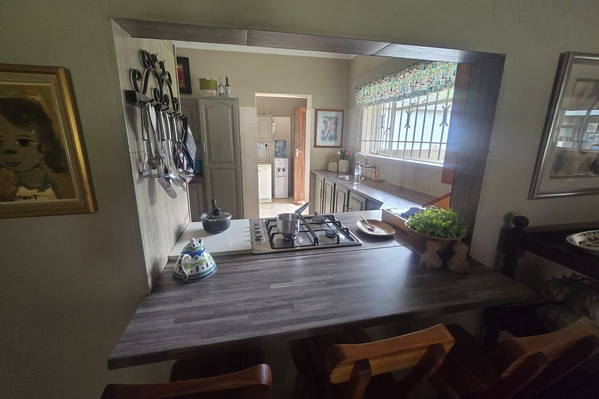 A functional kitchen featuring a gas hob, laminate breakfast bar, and ample cabinetry, with a pass-through window connecting to the adjacent living area.