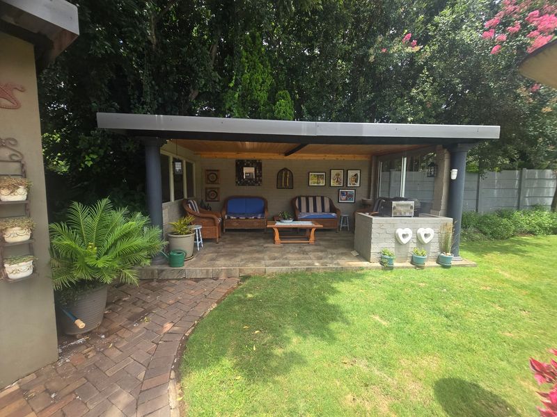 A covered outdoor patio area featuring a built-in braai, tiled flooring, and a solid roof structure, overlooking a landscaped garden.
