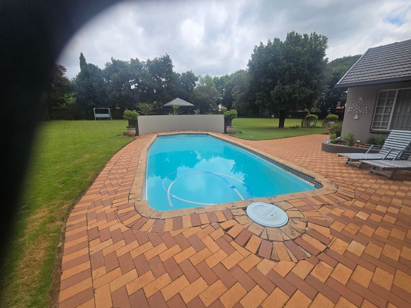 Outdoor pool area featuring a swimming pool surrounded by brick paving and a landscaped garden with a retaining wall.