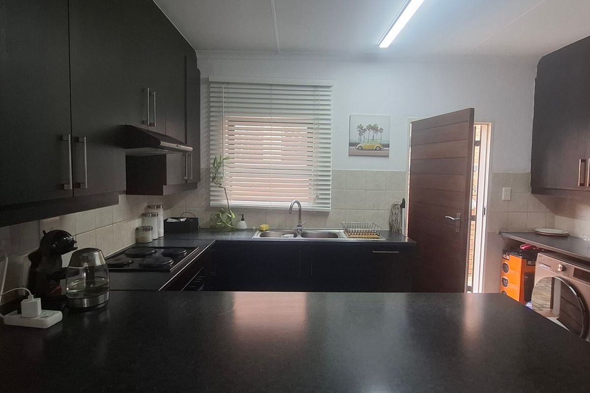 Functional kitchen featuring dark cabinetry, contrasting countertops, built-in appliances, and a tiled splashback with direct access to an exterior area.