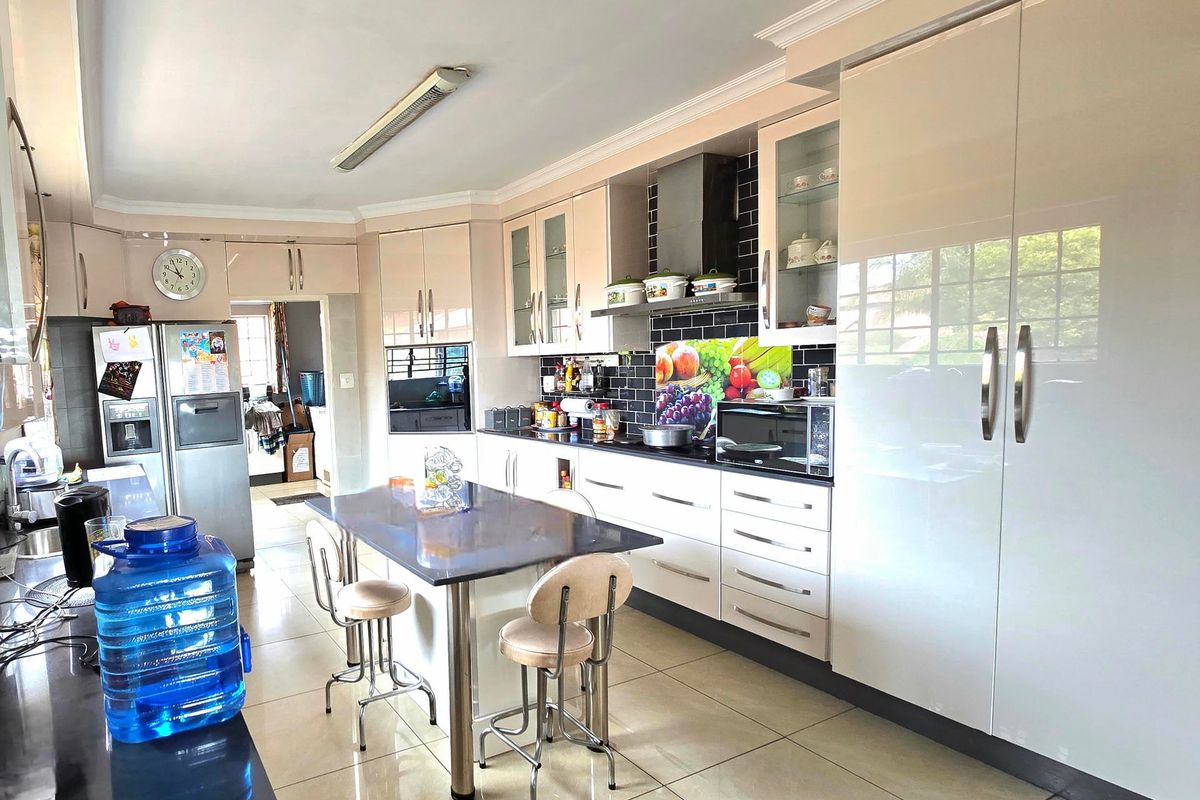 Modern kitchen featuring high-gloss cabinetry, a central island, built-in oven, extractor fan, and tiled flooring with a subway tile backsplash.