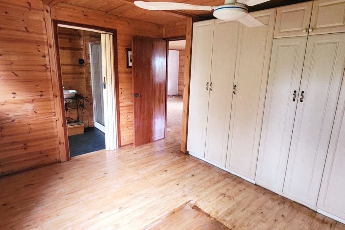 A bedroom featuring timber wall paneling, built-in cupboards, and a ceiling fan, with an adjacent bathroom visible through the doorway.