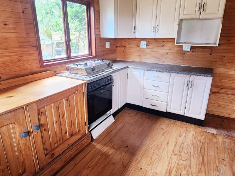 A functional kitchen featuring timber wall paneling, wooden flooring, white cabinetry, and a built-in oven with a gas hob.