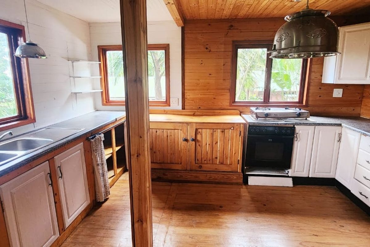 A rustic kitchen featuring timber wall paneling, wooden cabinetry, a gas hob, built-in oven, and double basin sink with ample natural light.