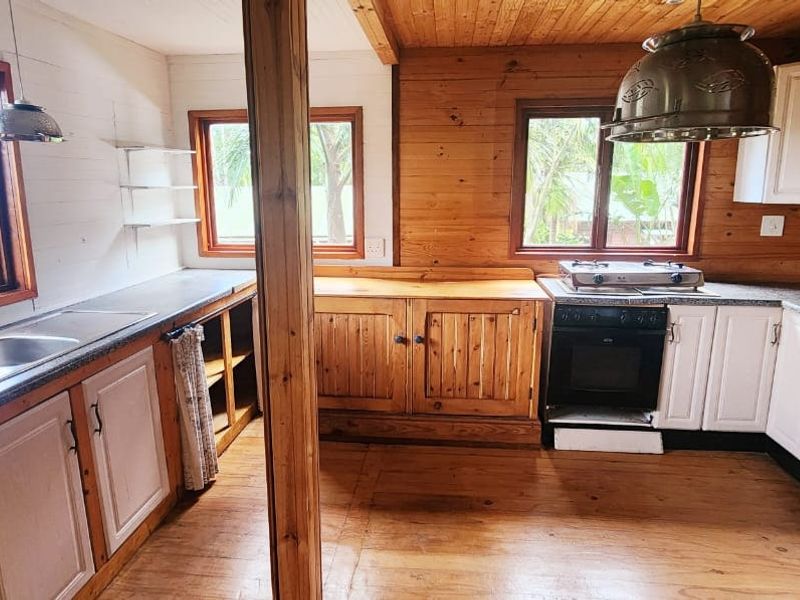 A rustic kitchen featuring timber wall paneling, wooden cabinetry, a gas hob, built-in oven, and double basin sink with ample natural light.