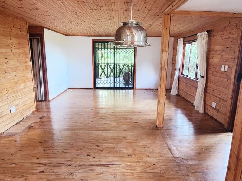 Spacious living area featuring extensive timber wall and ceiling paneling, polished timber flooring, and a security gate leading to the exterior.