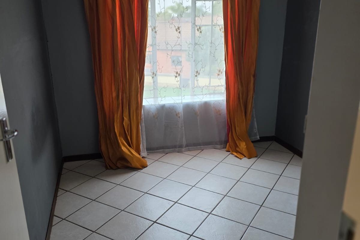 A vacant bedroom featuring neutral tiled flooring and a window with curtains, offering a clean and versatile space ready for personalization.