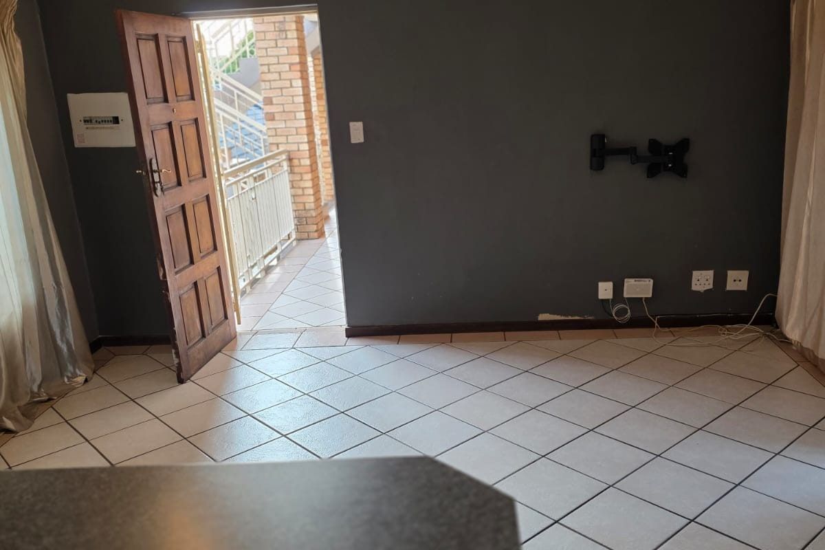An empty living room featuring ceramic floor tiles, dark grey walls, and direct access to an exterior balcony through a wooden door.