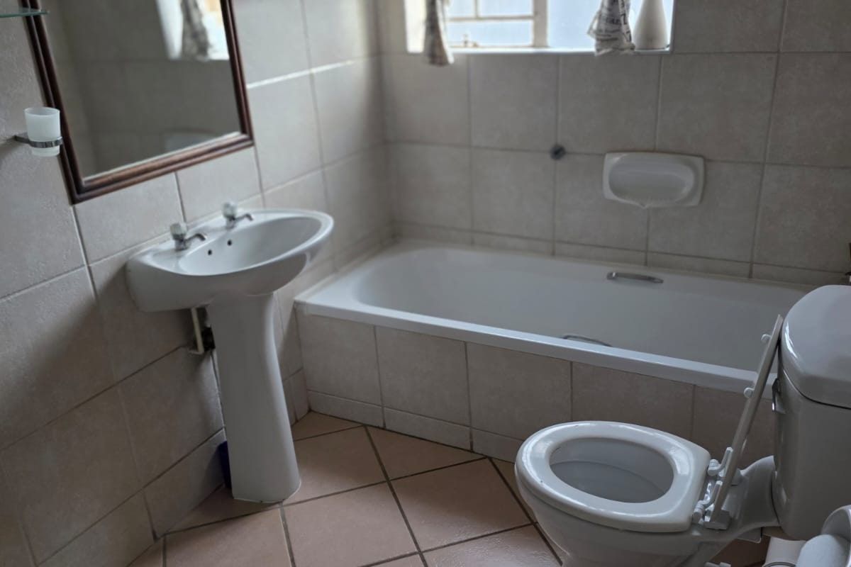A functional bathroom featuring a pedestal basin, built-in bathtub, and toilet with tiled finishes throughout.