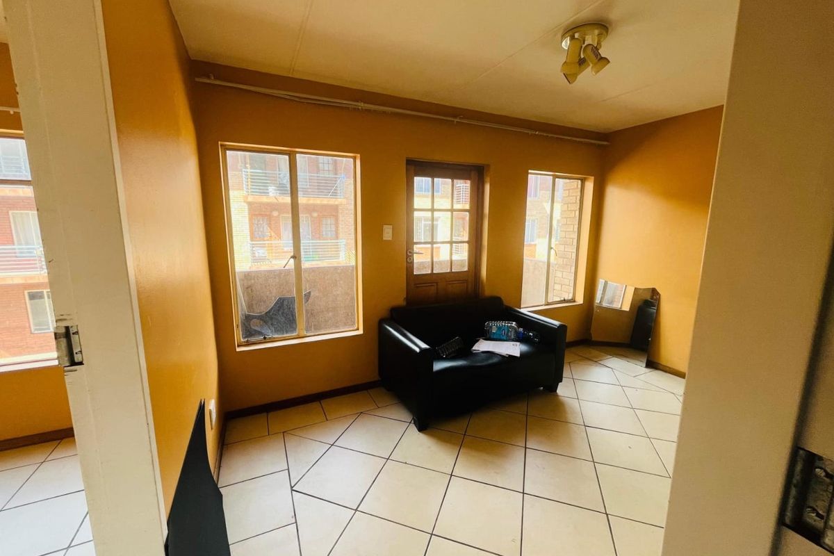 A living area featuring tiled flooring, large windows, and a glass-panelled door leading to an outdoor space, requiring cosmetic updates to improve its appeal.