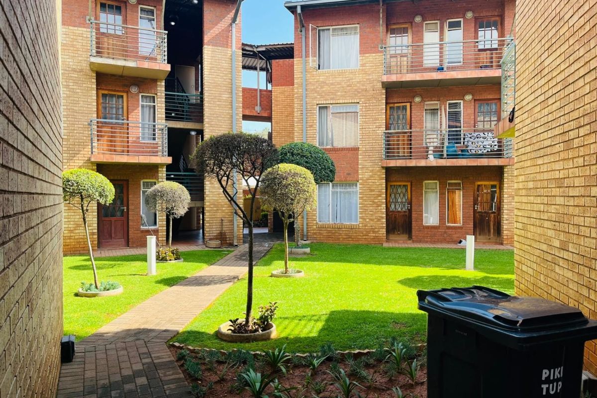A view of the apartment complex courtyard featuring brick facades, multiple balconies with metal railings, and a well-maintained central garden with paved walkways.