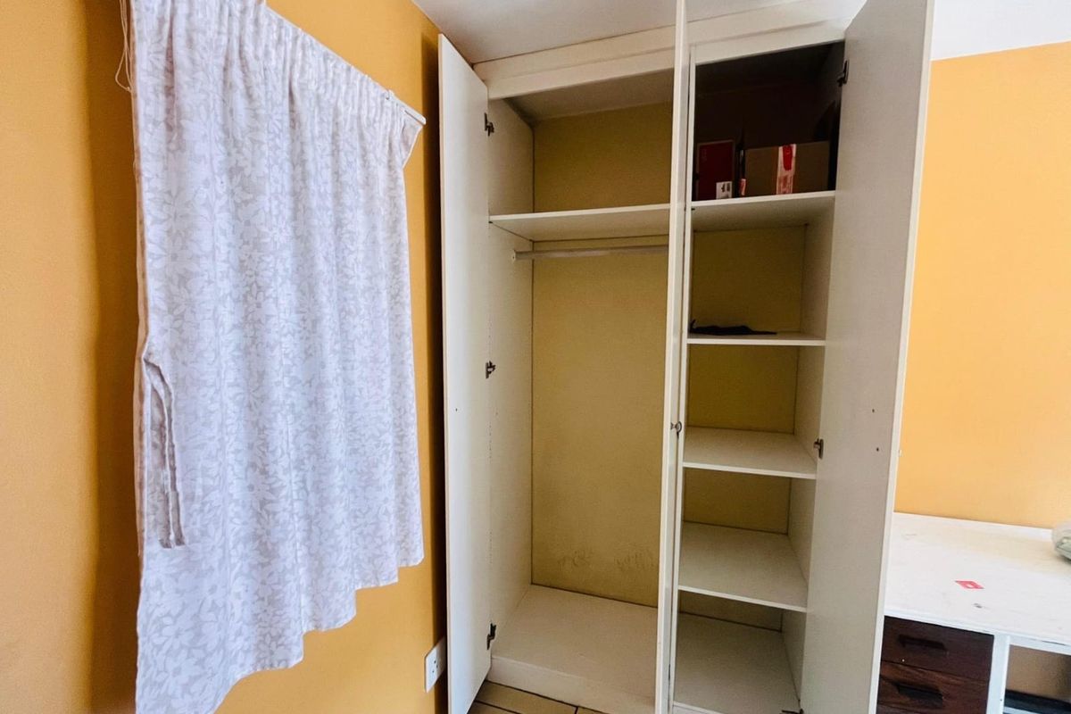 A bedroom featuring a built-in white wardrobe with shelving and hanging space, set against yellow walls with tiled flooring.