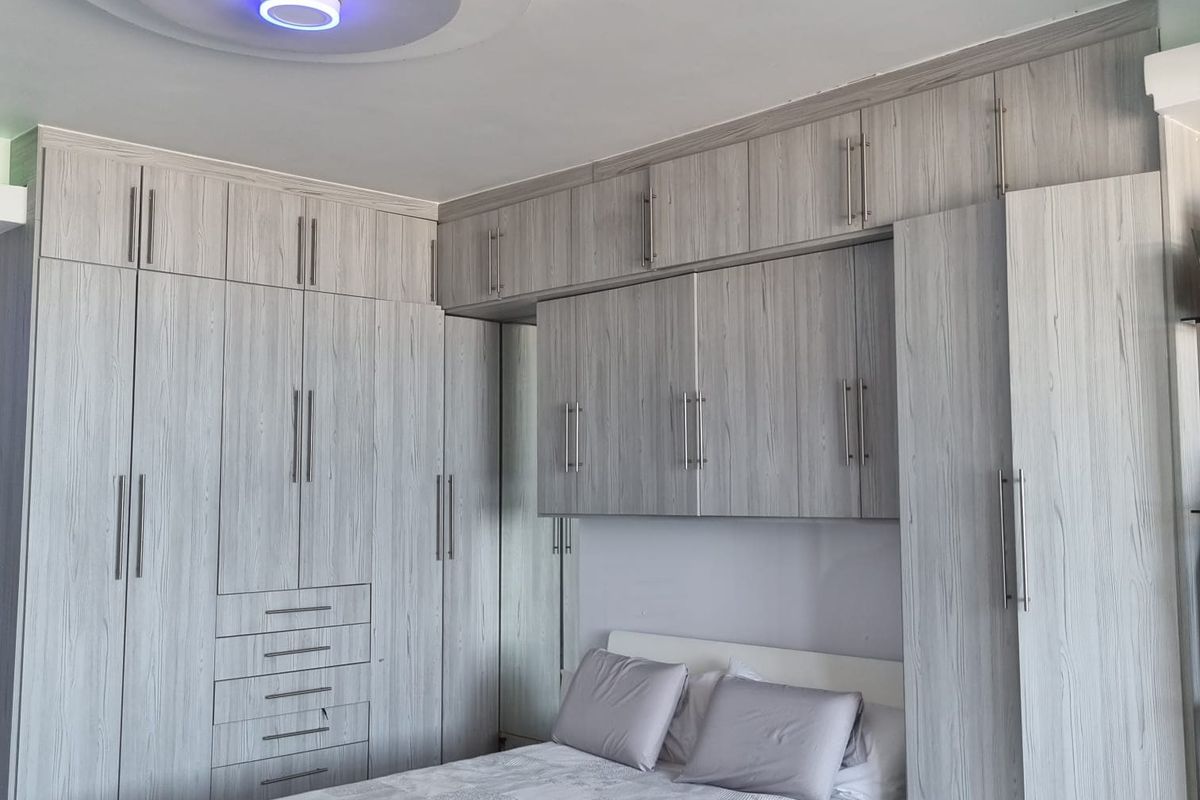 A well-appointed bedroom featuring extensive built-in cabinetry with light wood-grain finish, overhead storage, and a modern circular recessed ceiling light fixture.