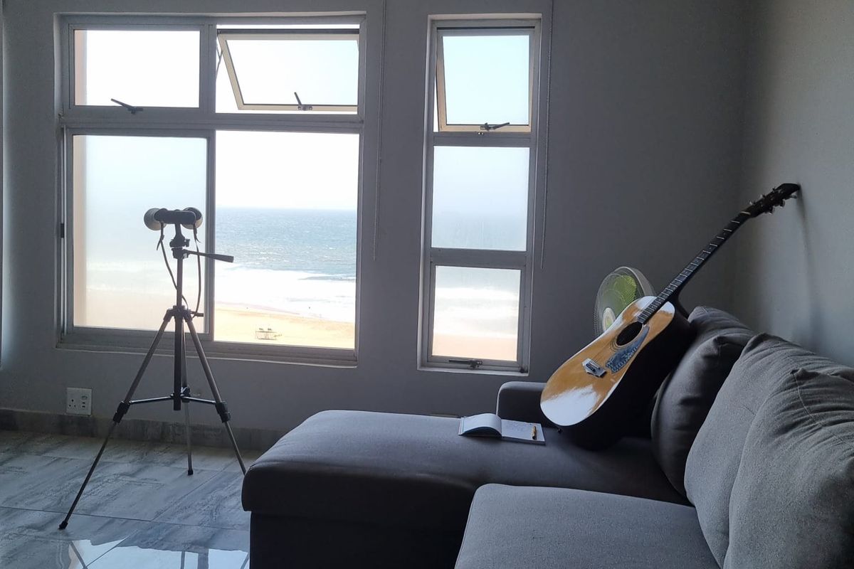 A bright living room featuring large windows with direct ocean views, polished tile flooring, and neutral wall finishes.