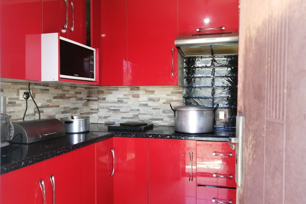 A compact kitchen featuring vibrant red high-gloss cabinetry, black granite countertops, and a combination of stone-look and black subway tile backsplashes.