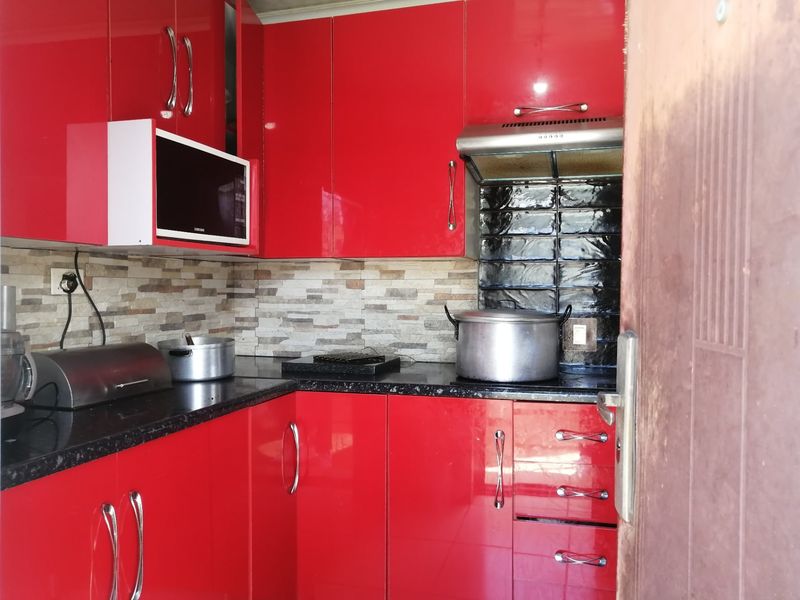 A compact kitchen featuring vibrant red high-gloss cabinetry, black granite countertops, and a combination of stone-look and black subway tile backsplashes.